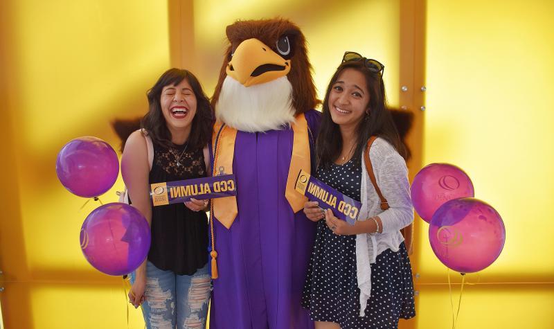 Two CCD Students holding an Alumni bumpersticker with the mascot